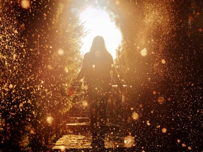 rear view of woman silhouette looking at the light from the end of the tunnel, being surrounded by shiny golden lights.